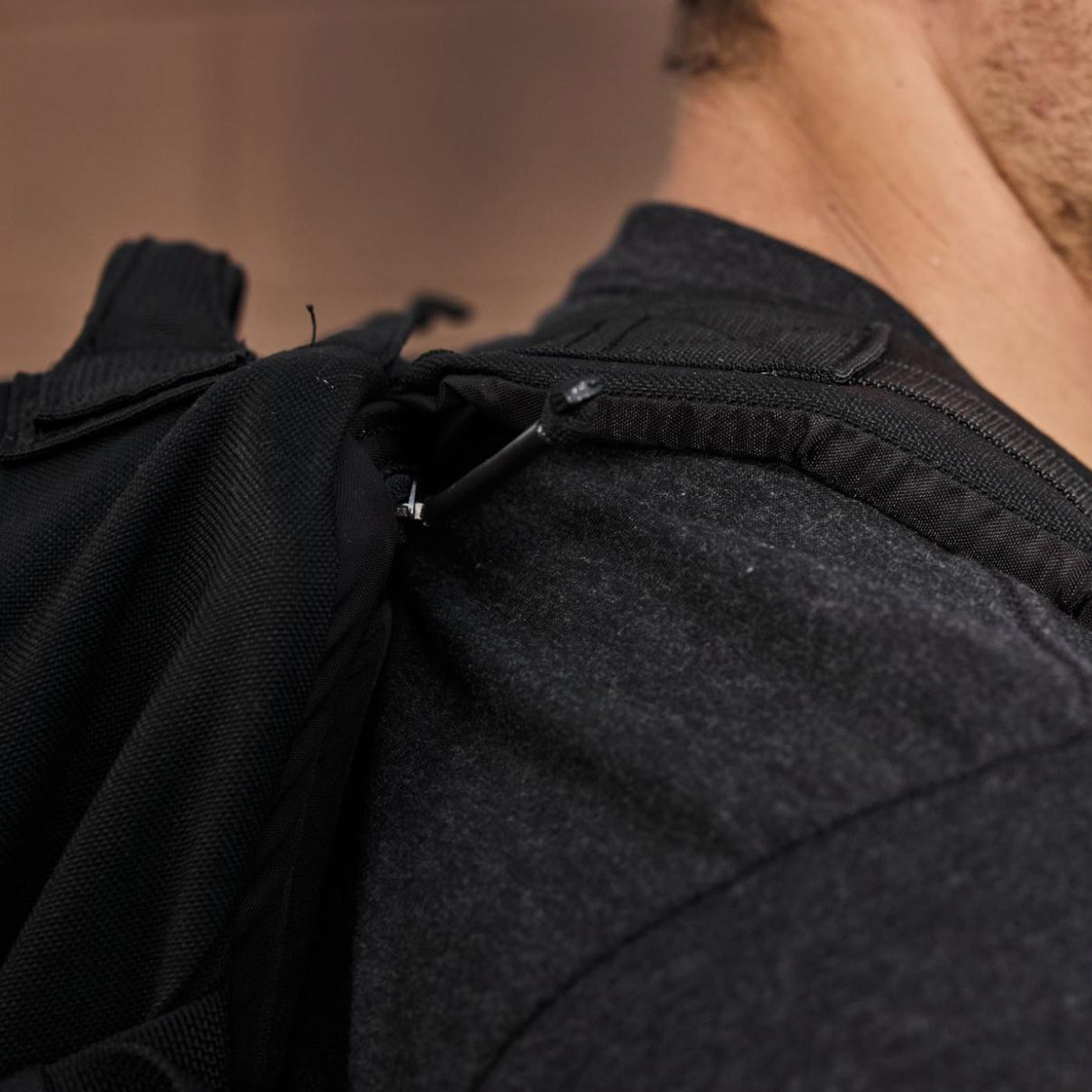 Close-up of a black backpack strap on a person's shoulder, with part of their neck and shirt visible.