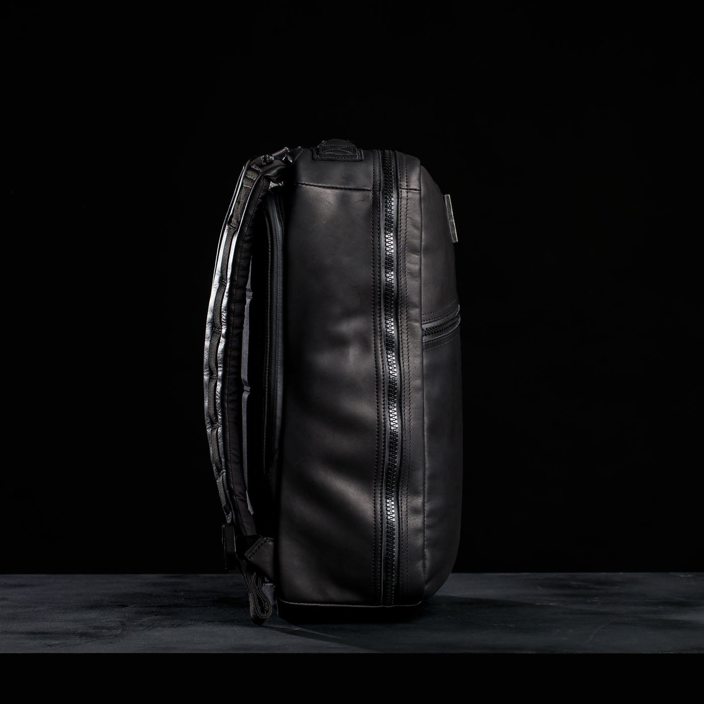 The GR1 USA x Carryology - Berserker Viking backpack in black leather stands upright on a dark surface against a black background, channeling the spirit of Viking warriors.