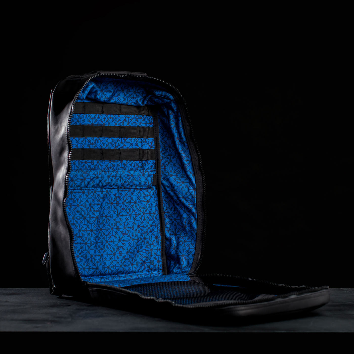 Open black GR1 USA x Carryology - Berserker Viking backpack with a blue patterned interior and sturdy black straps, displayed against a dark background.