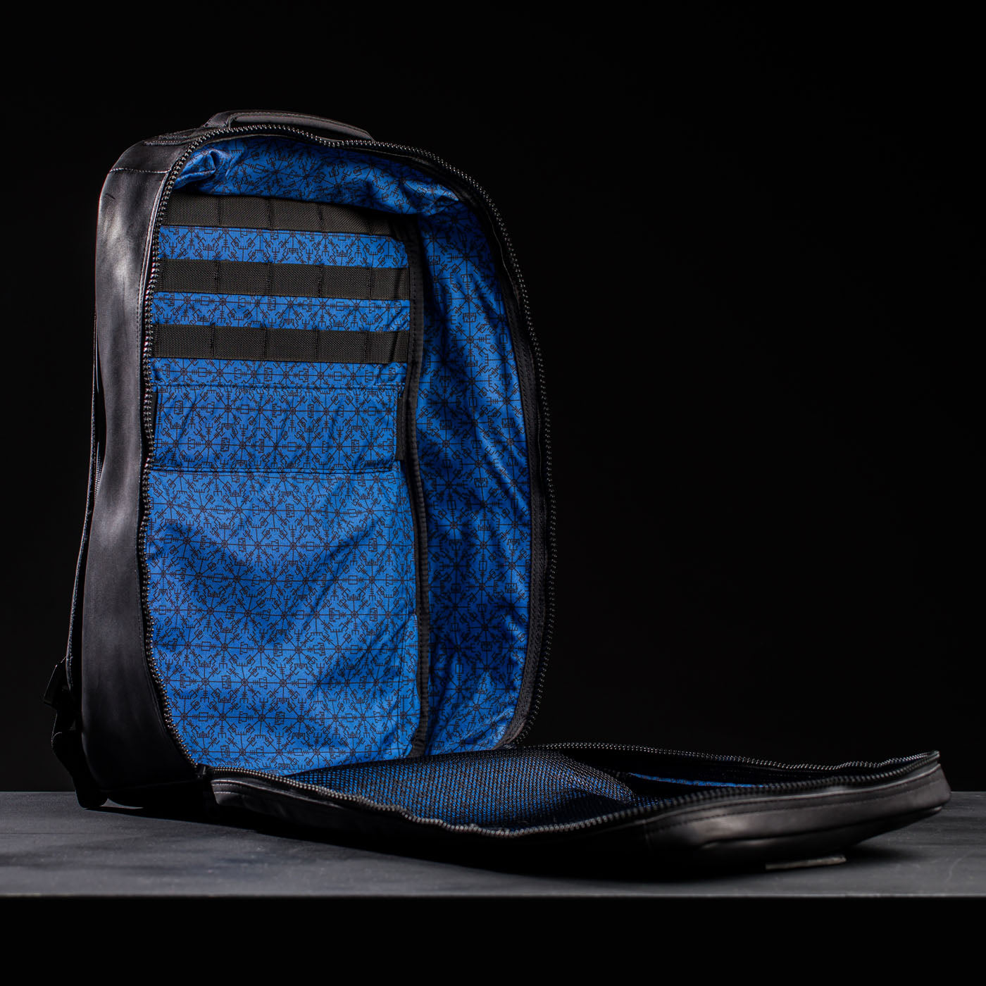 Open black GR1 USA x Carryology - Berserker Viking backpack with blue geometric-patterned interior, evoking Norsemen warriors’ bold style, displayed against a dark background.