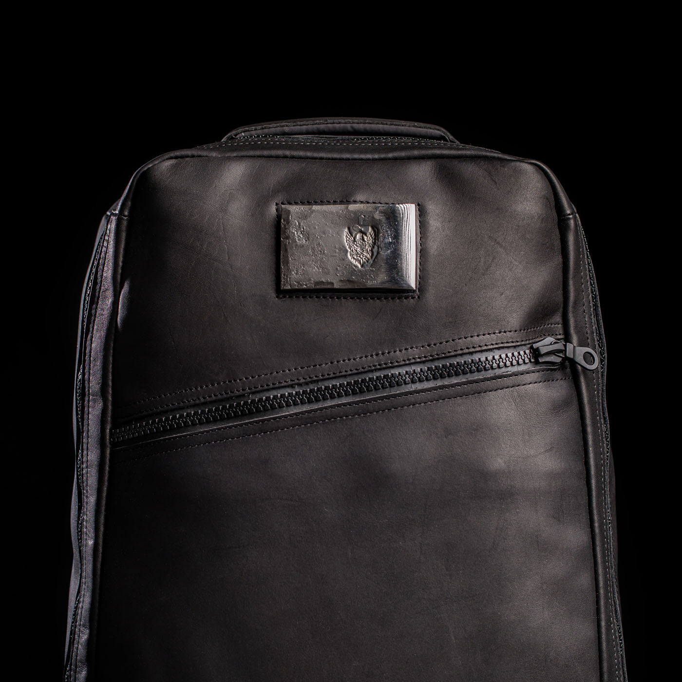 The GR1 USA x Carryology - Berserker Viking backpack features black leather, a slanted zipper pocket, a small patch logo, and is inspired by Viking armor, all set against a black background.