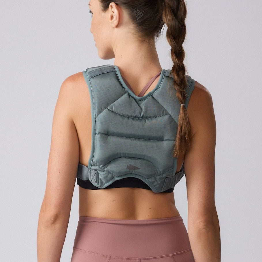 Woman with a braid wearing a gray weighted vest and pink leggings, shown from the back against a plain background.