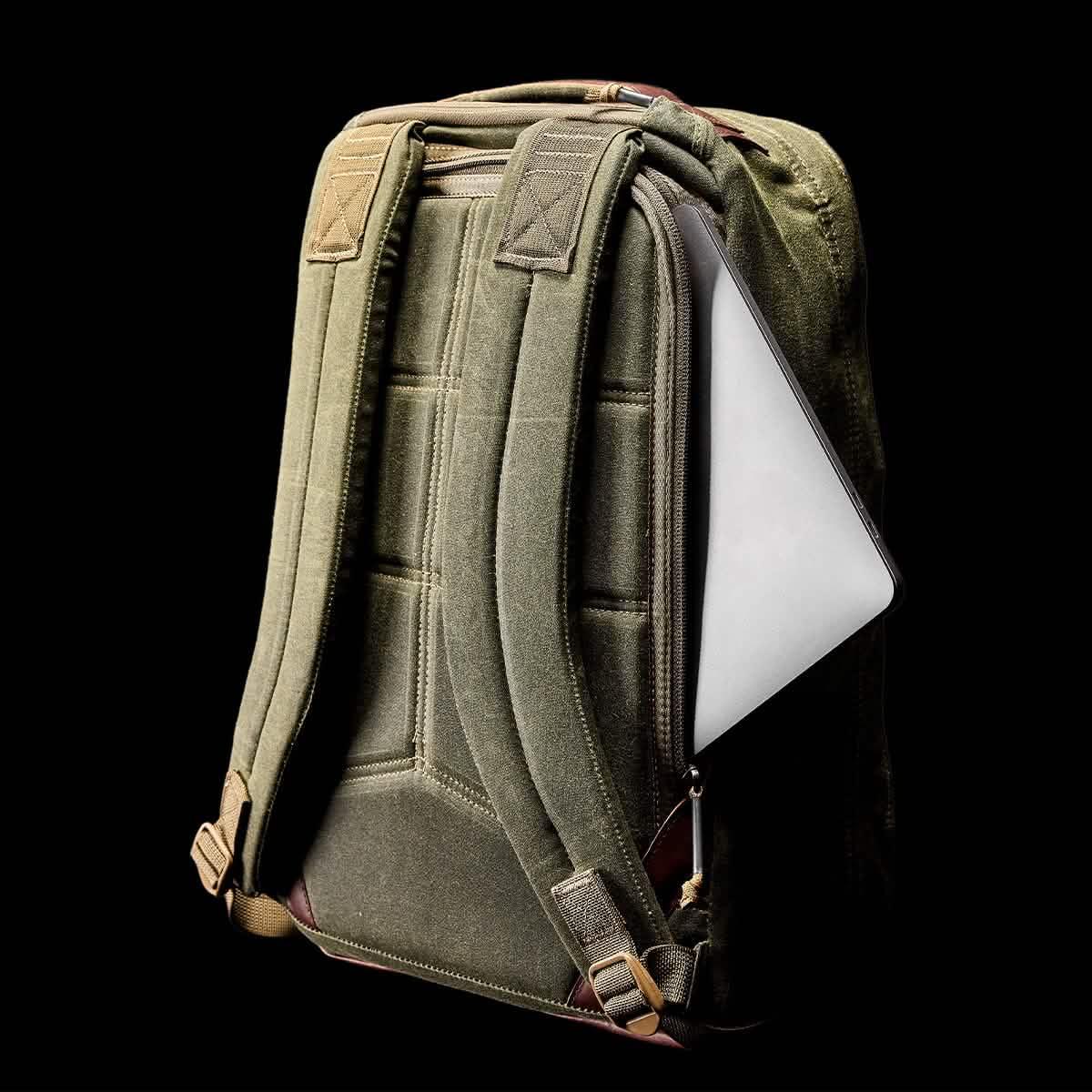 Olive green tactical backpack with padded straps and a laptop partially visible in side pocket on black background