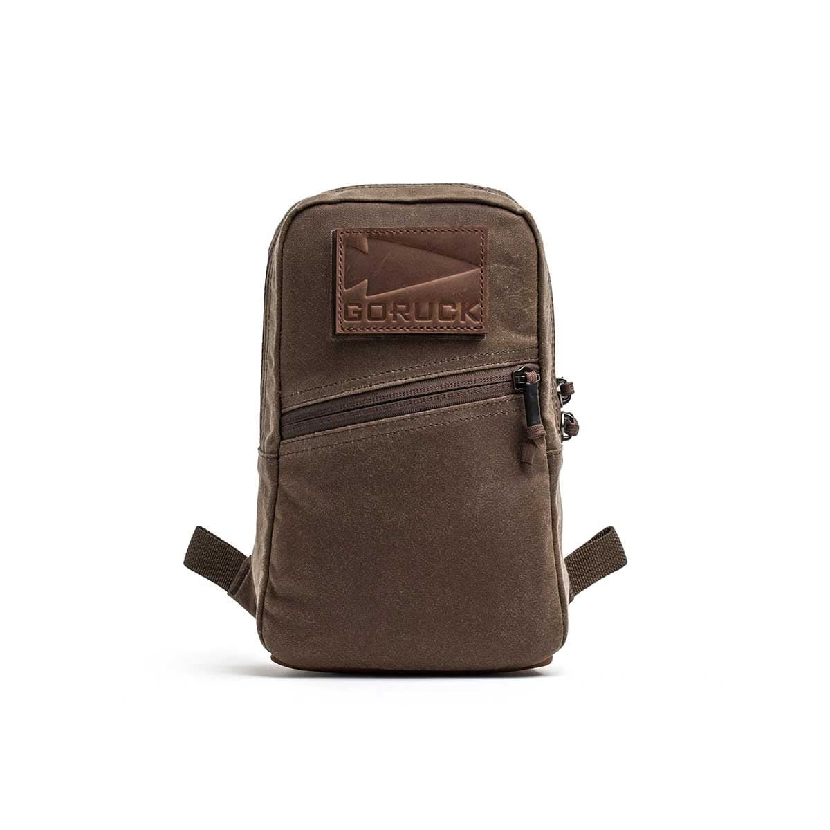 The Waxed Canvas GRenade, a small brown bag with a front zipper pocket and leather patch, is shown on a white background.