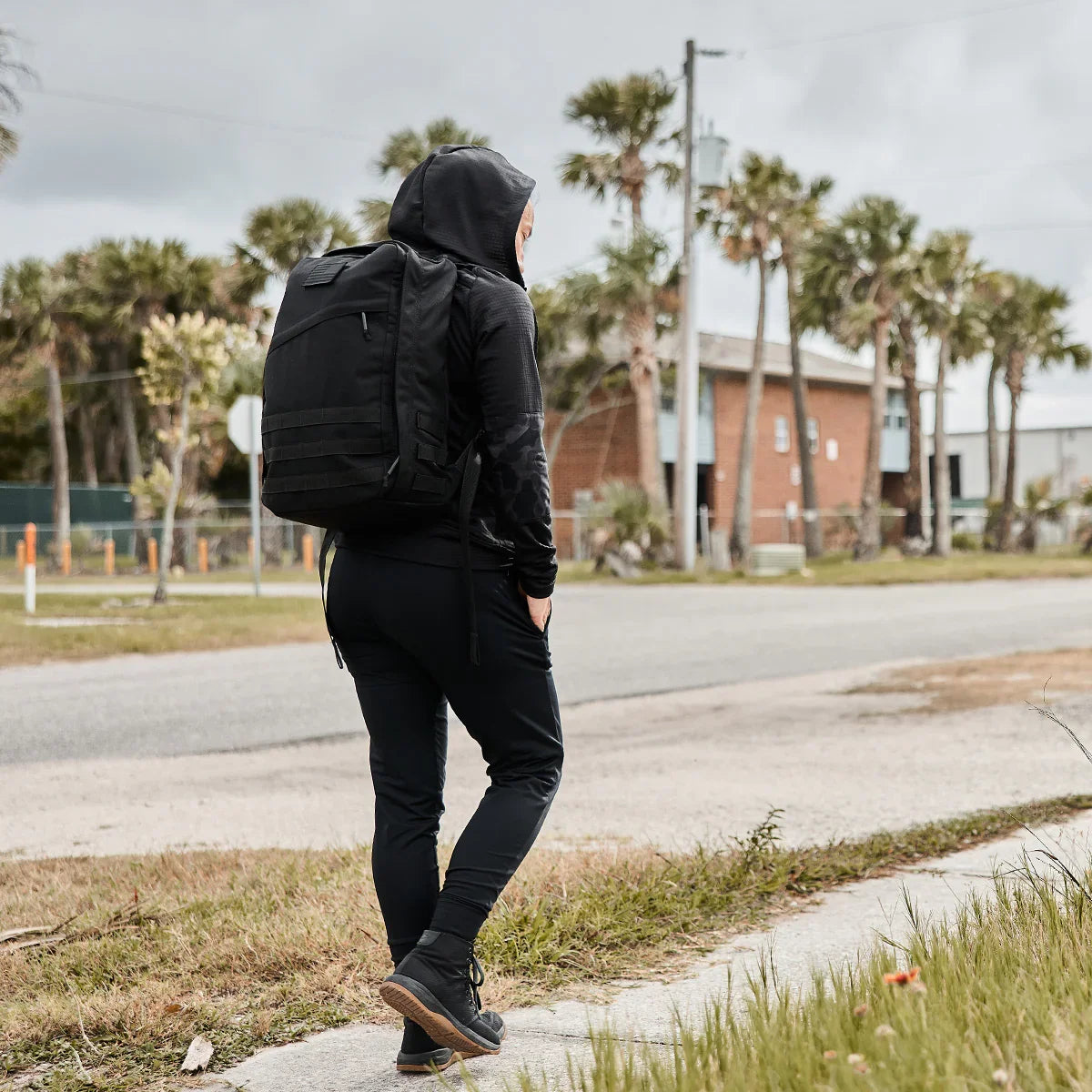 Person rucking in GORUCK grid fleece hoodie with large black backpack, urban street scene