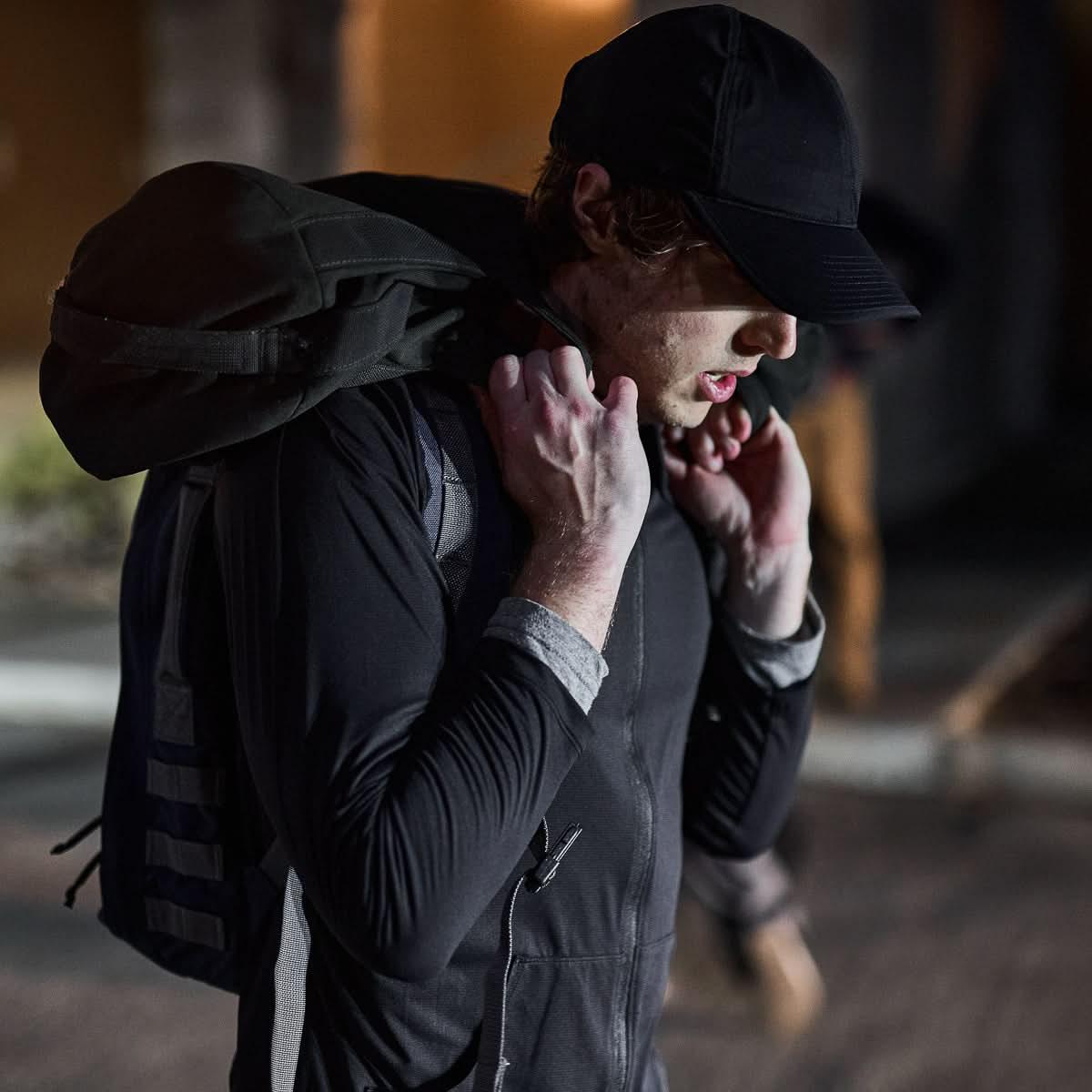 Man wearing black running hat and athletic jacket carrying a heavy backpack during outdoor night training