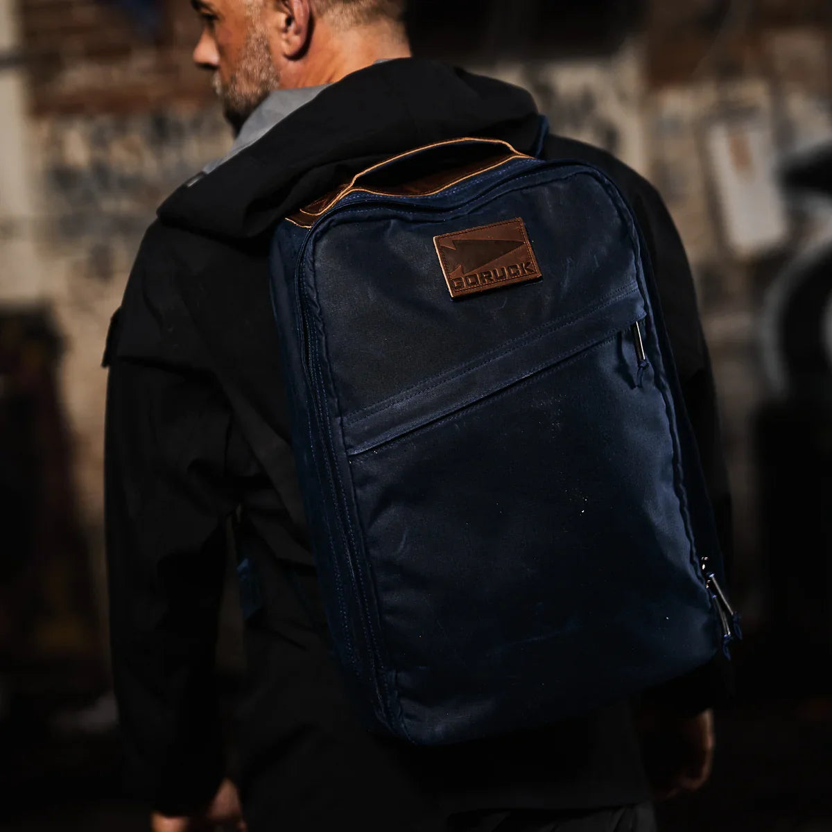 Man wearing a navy GORUCK backpack with leather logo patch in urban rugged setting