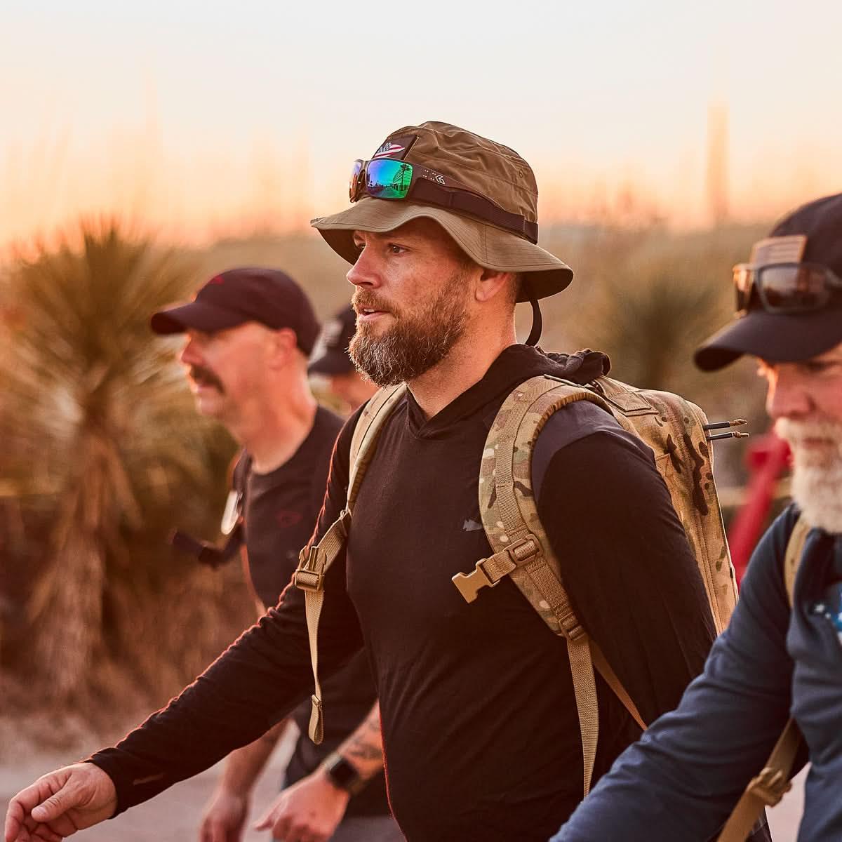 Man wearing GORUCK Ranger Green Boonie Hat with sunglasses and tactical backpack walking outdoors at sunset