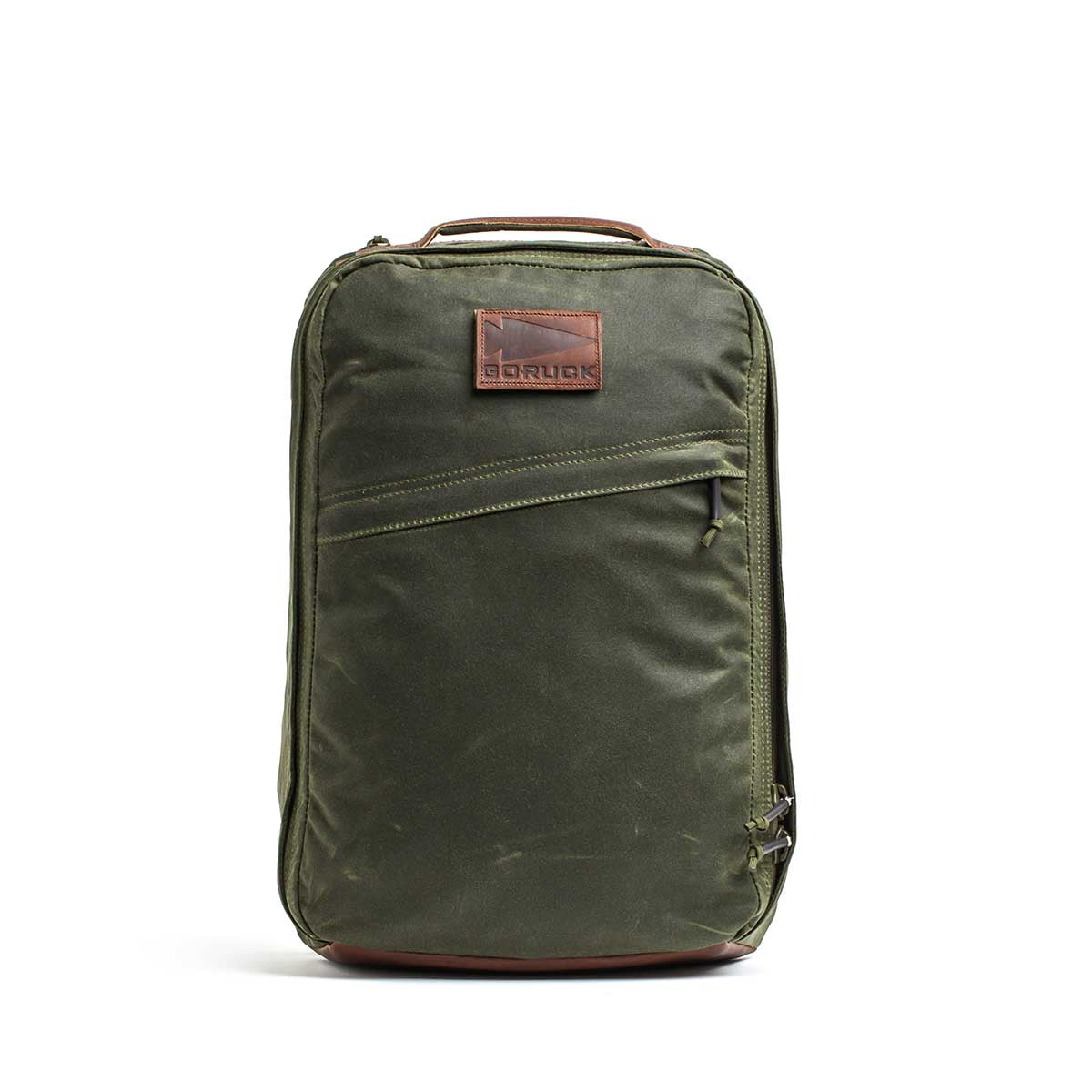 The GR1 USA - Heritage Waxed Canvas rucksack in olive green features a brown Red Wing Leather patch and a front diagonal zipper pocket, shown standing upright on a white background.