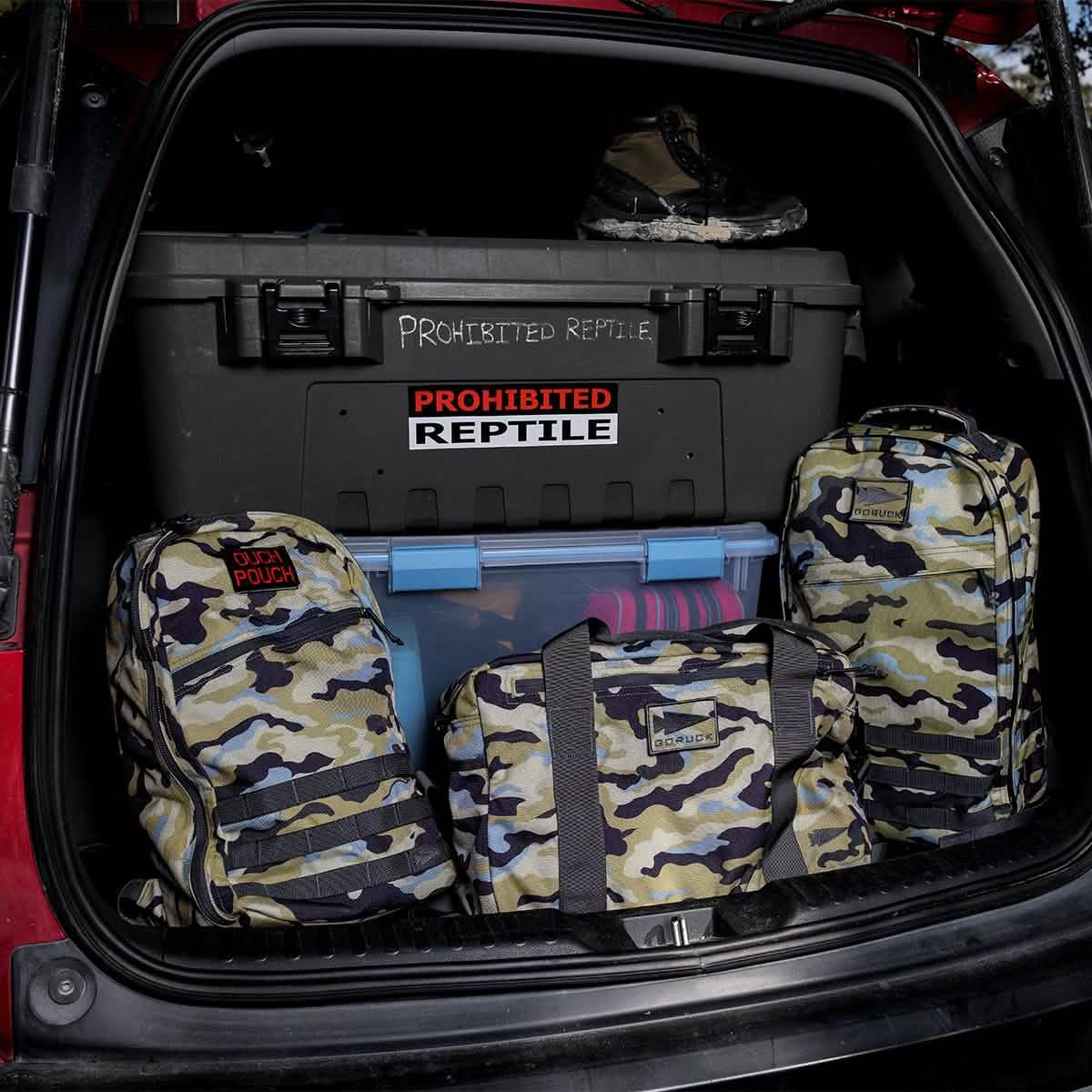 Open car trunk with GORUCK Everglades camo tactical bags and tough storage boxes labeled Prohibited Reptile