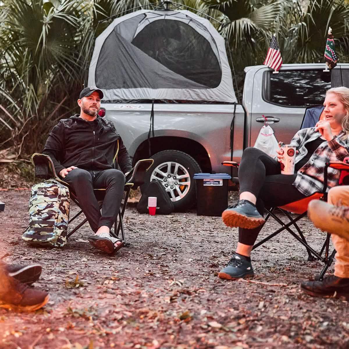 Two people camping with GORUCK gear near a truck with rooftop tent in a wooded setting