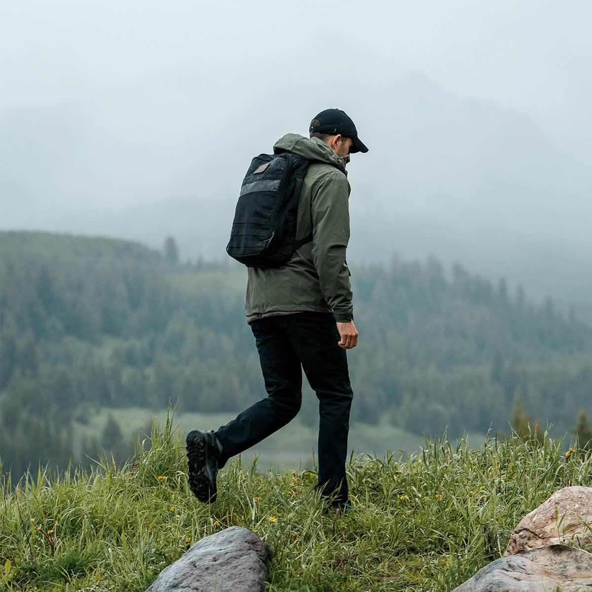 Man wearing black backpack and green jacket hiking in misty mountain forest landscape