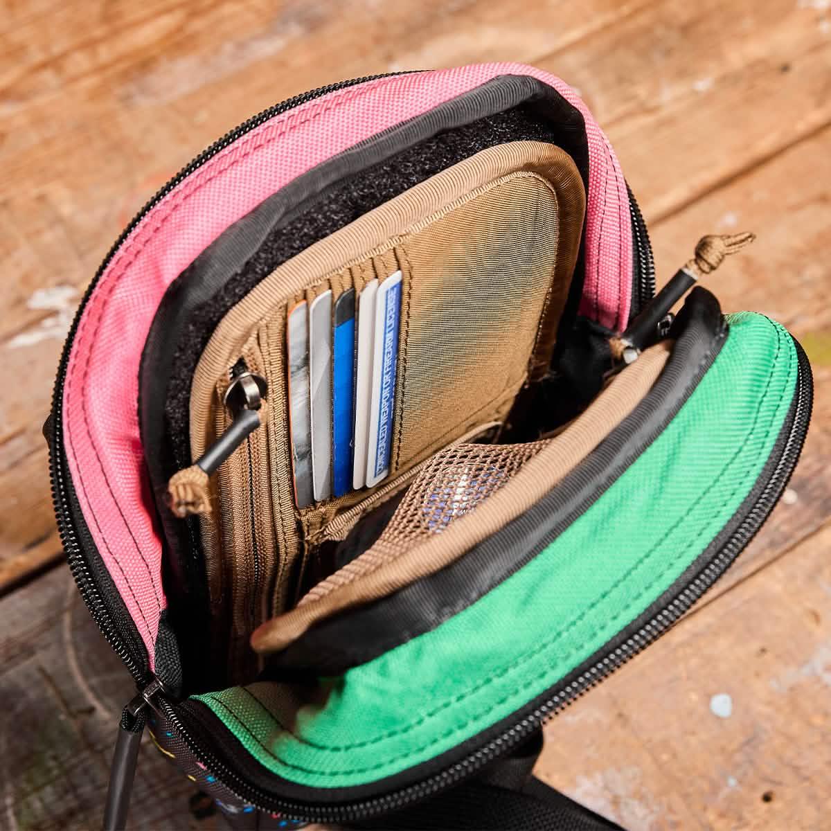 GORUCK ID card organizer with pink and green compartments holding cards and mesh pocket on wooden surface