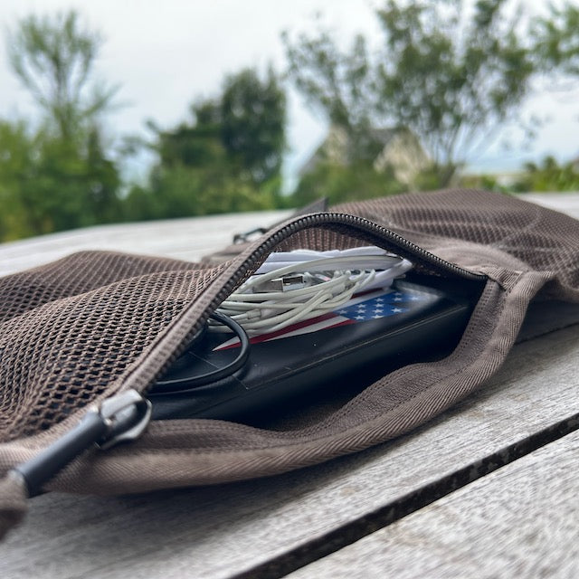 The Wire Dopp - Waxed Canvas rests on a wooden table, neatly storing a phone and earphones—ideal for your EDC essentials, with trees visible in the background.