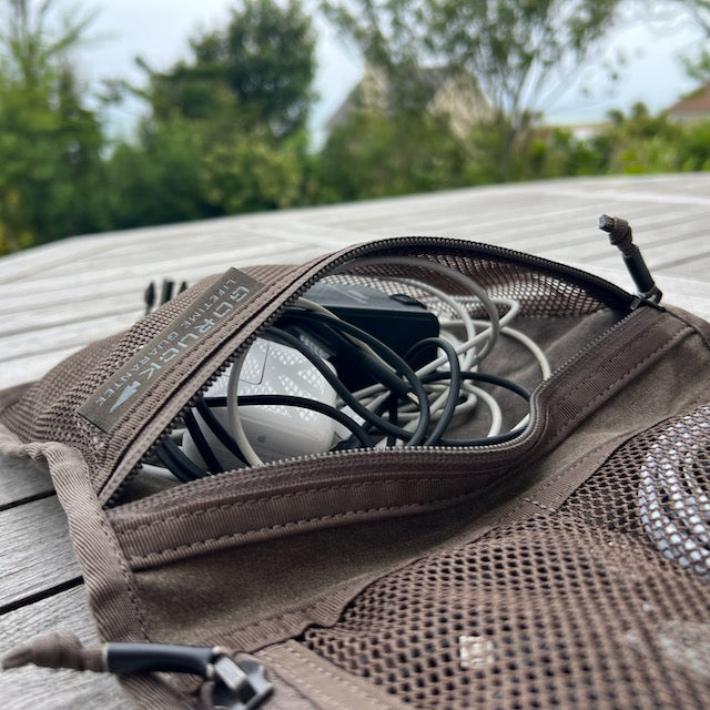 A Wire Dopp - Waxed Canvas organizer filled with tangled cables and a mouse rests on a wooden outdoor table.