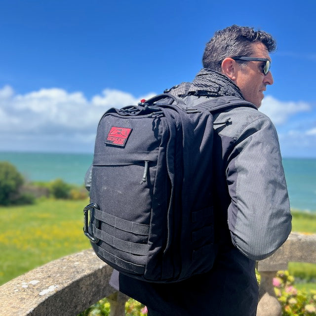 Man with sunglasses and the GR2 ruck stands by a stone railing overlooking the ocean, ready for one bag travel.