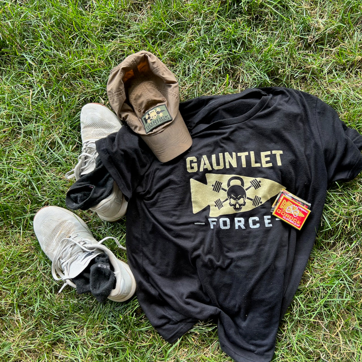 A black “Gauntlet Force” shirt, tan cap, white sneakers with Merino Challenge Socks - Ankle (No-Show), and a patch on green grass.