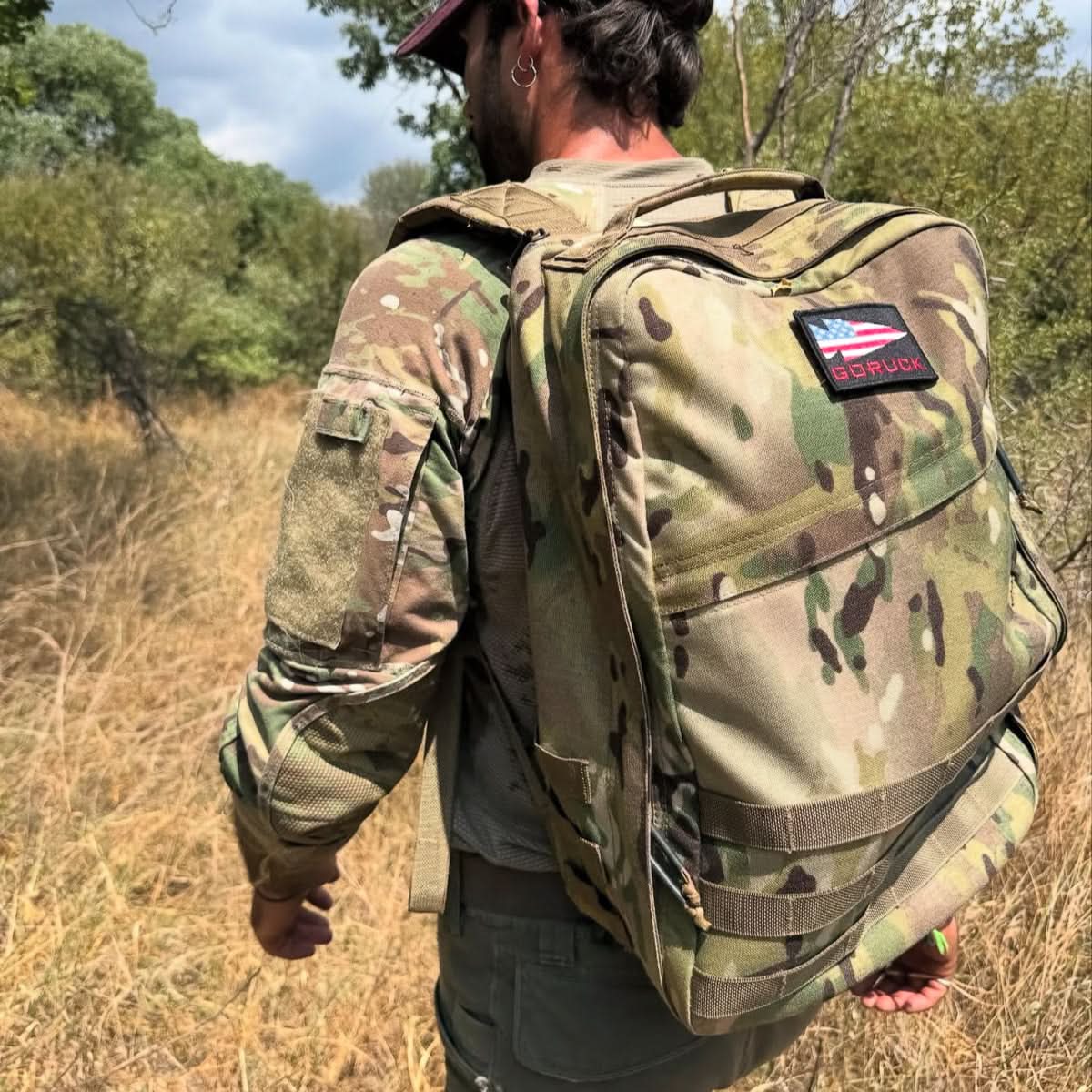 Dressed in camo, a person walks outdoors through grassy woods carrying the GR1 USA - Ballistic Nylon Cordura (The Original Ruck) everyday rucksack.