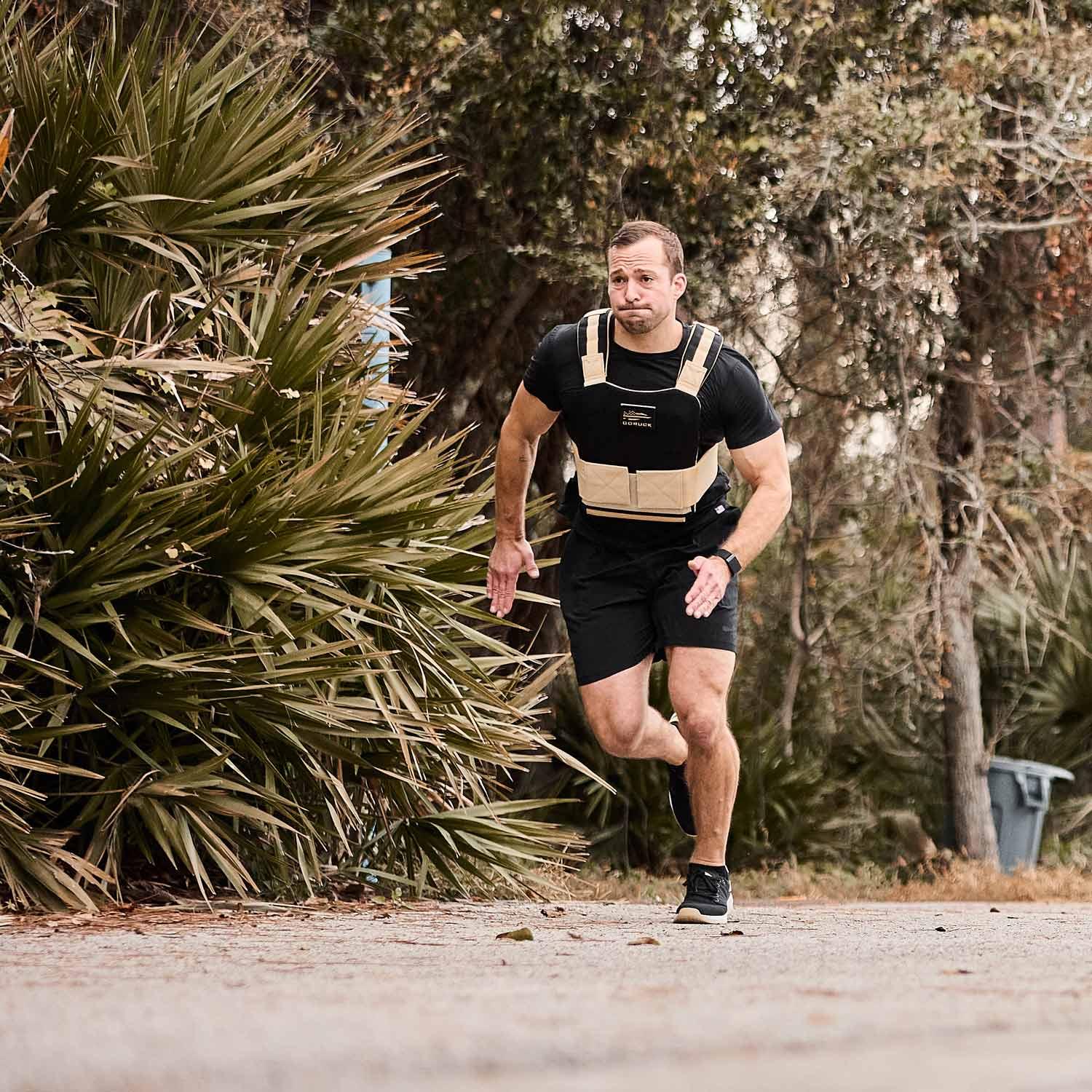 Athletic man running outdoors wearing GORUCK weighted vest training on a trail surrounded by trees