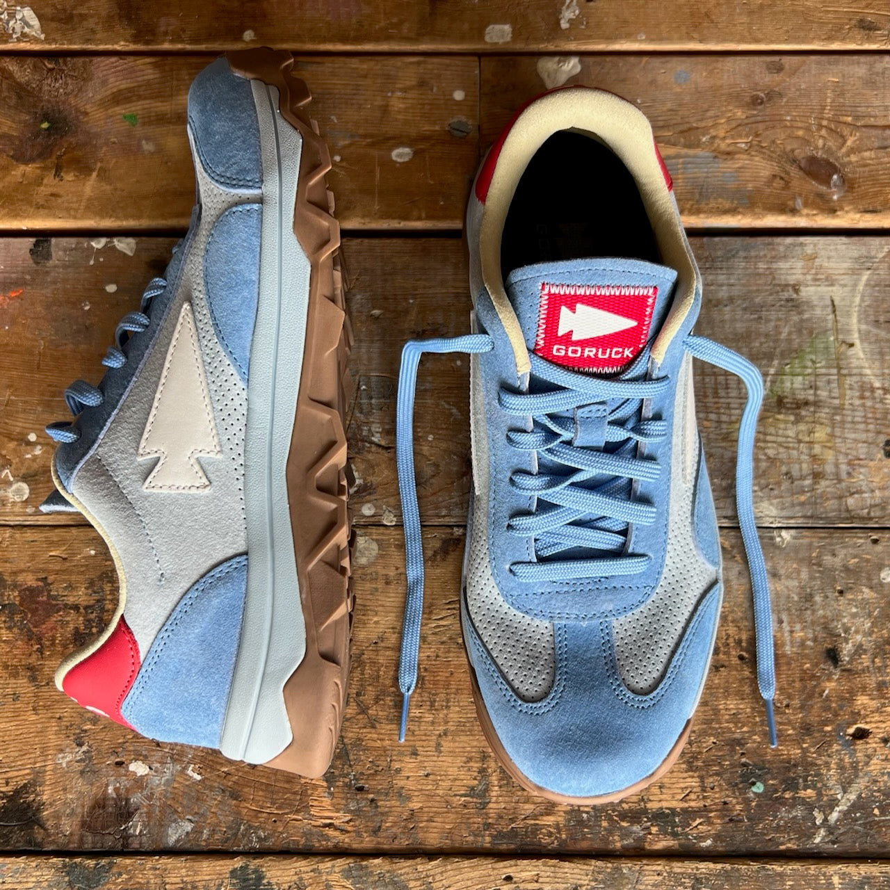 A pair of Mackall 45 Americana sneakers in blue with white and red accents displayed on a worn wooden surface.