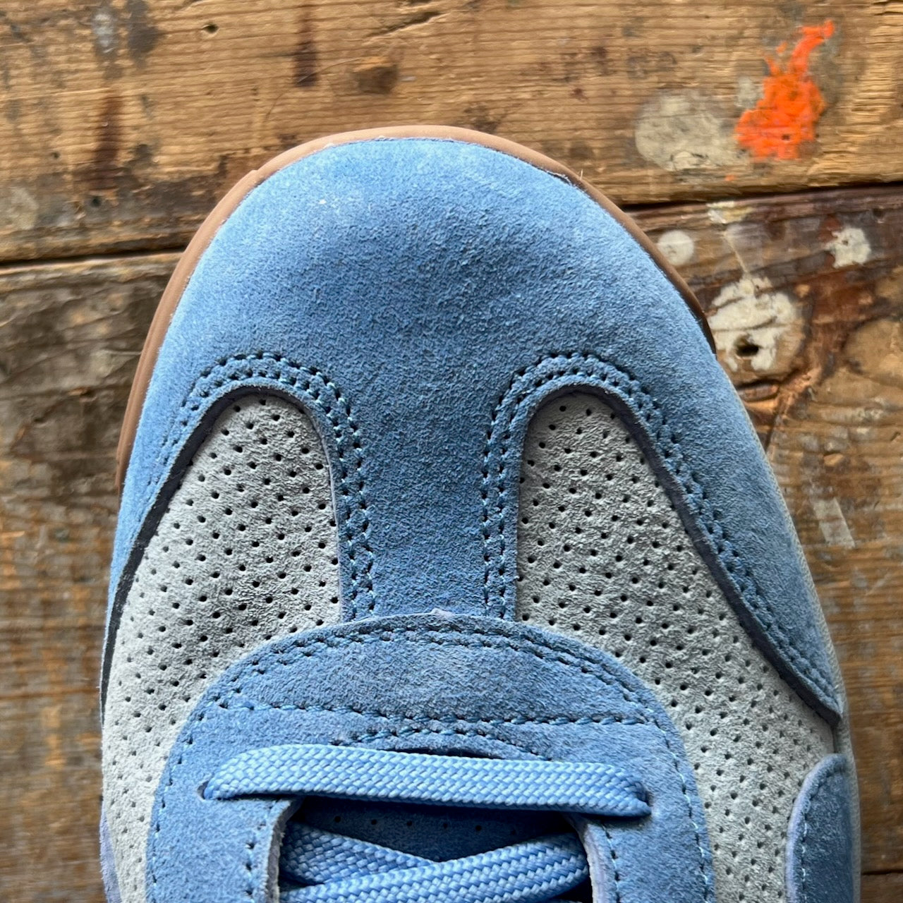 Close-up of the Mackall 45 Americana blue suede sneaker displayed on a worn wooden surface with a small orange paint spot.
