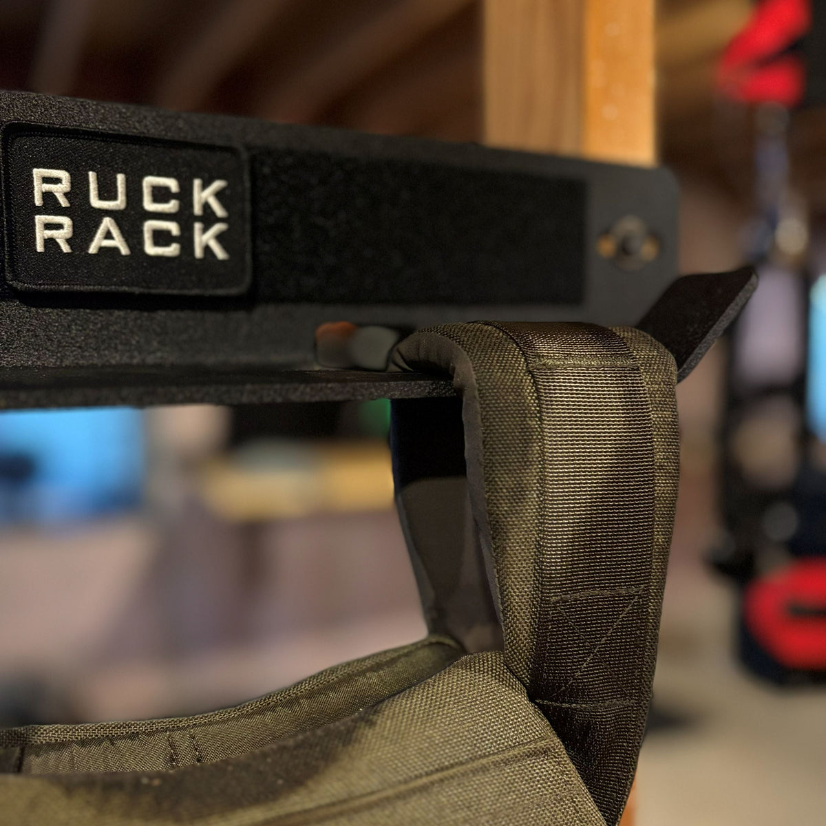A black Ruck Rack wall-mounted storage rack with a weighted backpack strap hanging from its hook.