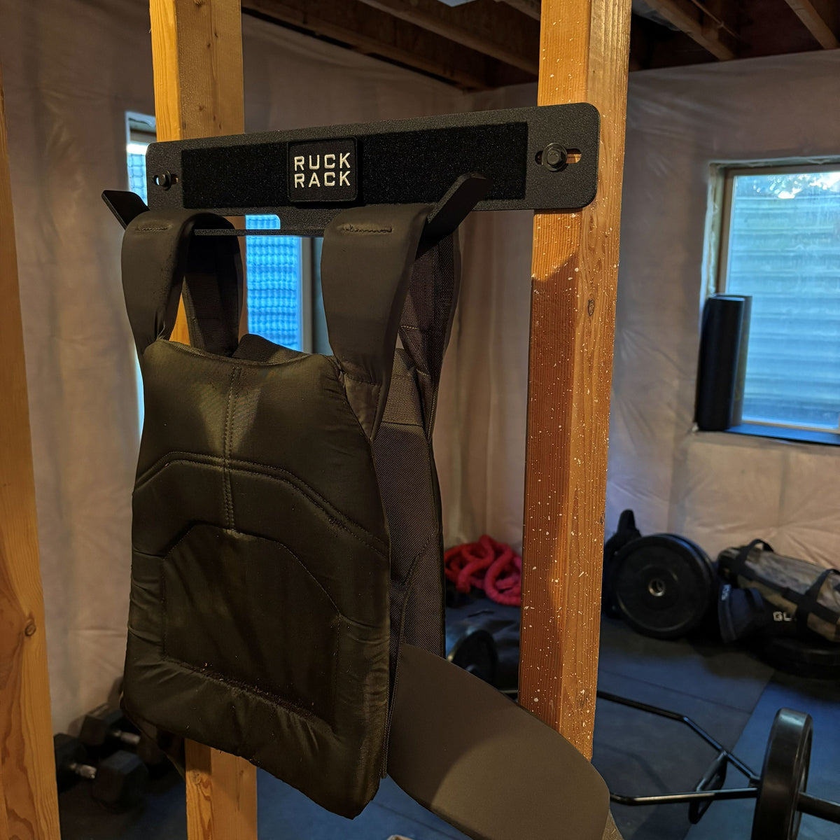 Black weighted vest hanging on a wall-mounted storage rack designed for tactical gear organization.