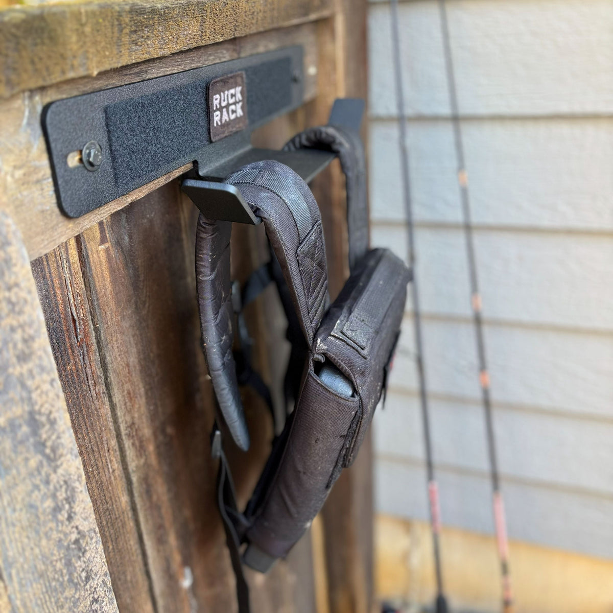 A black Ruck Rack wall-mounted storage rack with a weighted vest hanging on a wooden surface.