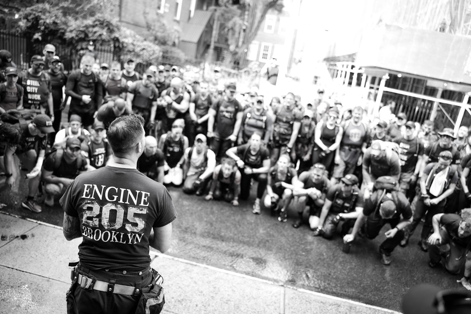 A firefighter addresses a large group of kneeling people outdoors in Brooklyn.