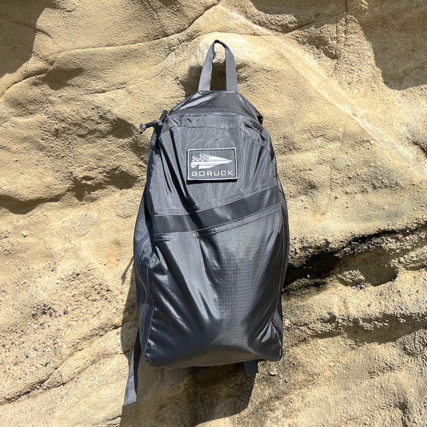 The Packable Bullet Ruck - Ripstop ROBIC® from GORUCK hangs on a textured tan rock wall in bright sunlight.