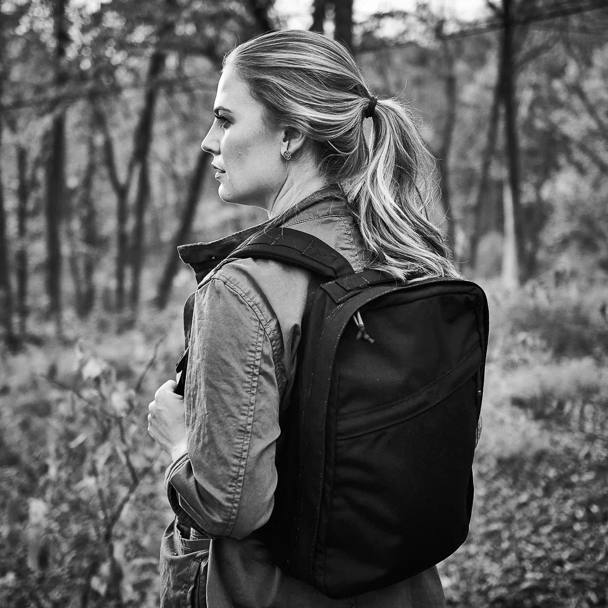 Woman wearing GORUCK backpack outdoors in forest, side profile, black and white photo