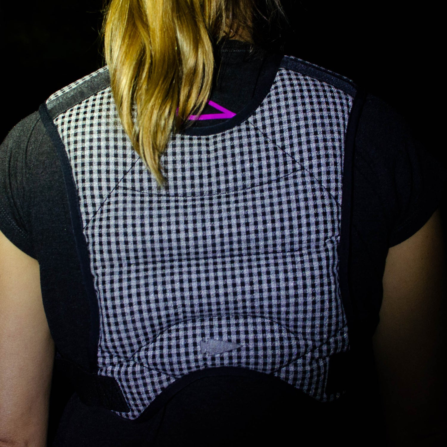 A person with blond hair, wearing a black shirt and the Spy Ruck | Women's Weighted Vest, featuring a checkered pattern, viewed from behind.