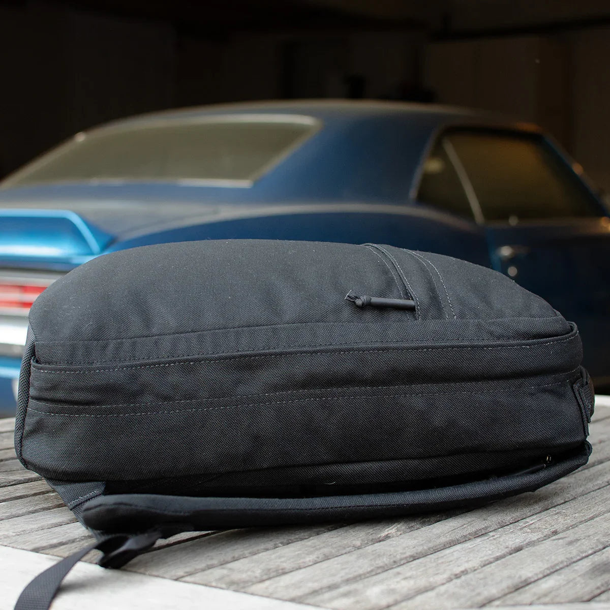 GORUCK black rucksack on wooden table with blue classic car in background
