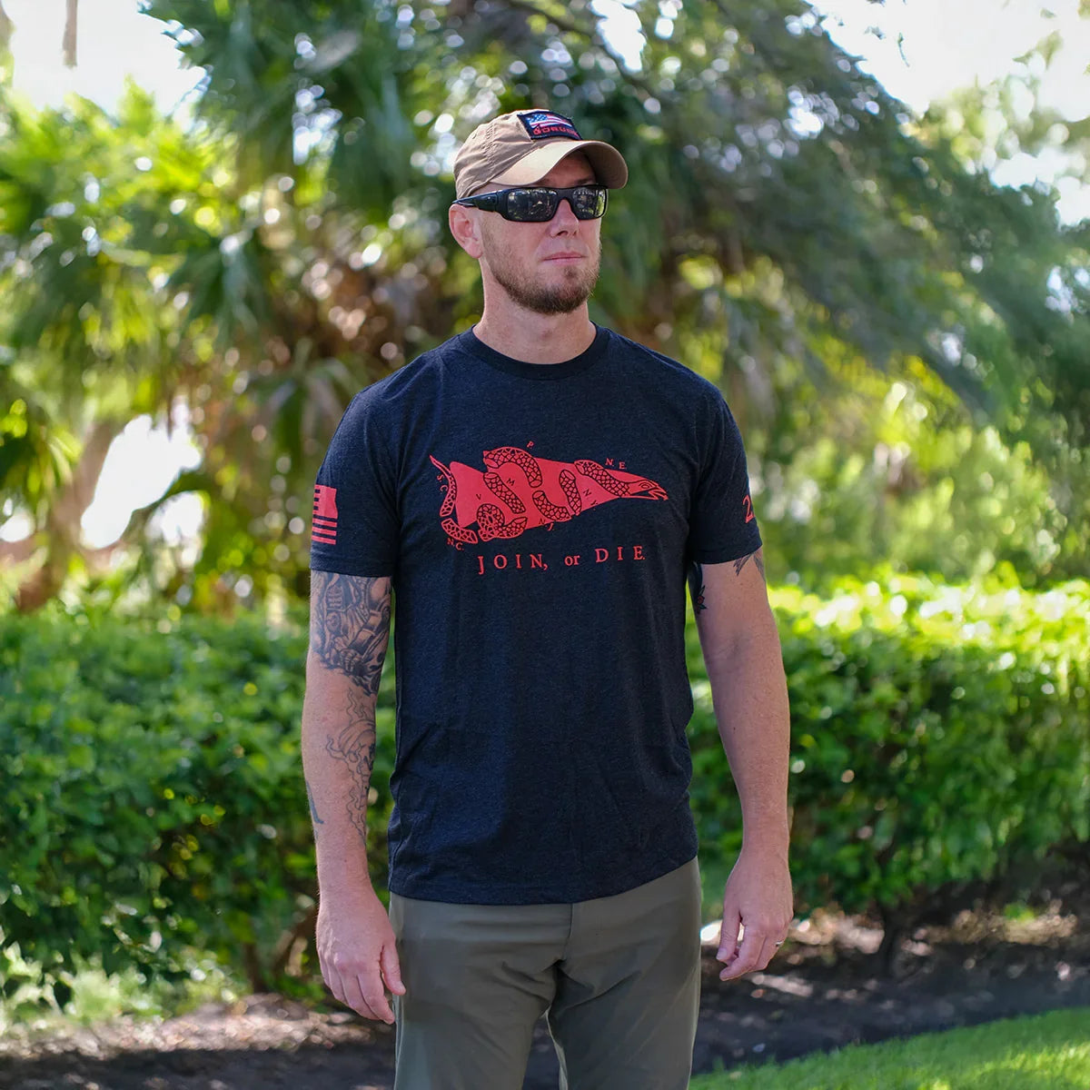 Man wearing black tactical 'Join or Die' GORUCK t-shirt with red snake graphic, outdoors by greenery