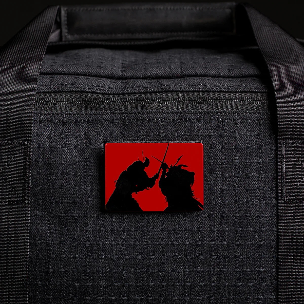 Rectangular pin with two samurai dueling on red, attached to the black Kit Bag x Carryology - GRXC2 Samurai 2.0, crafted from custom technical fabric.
