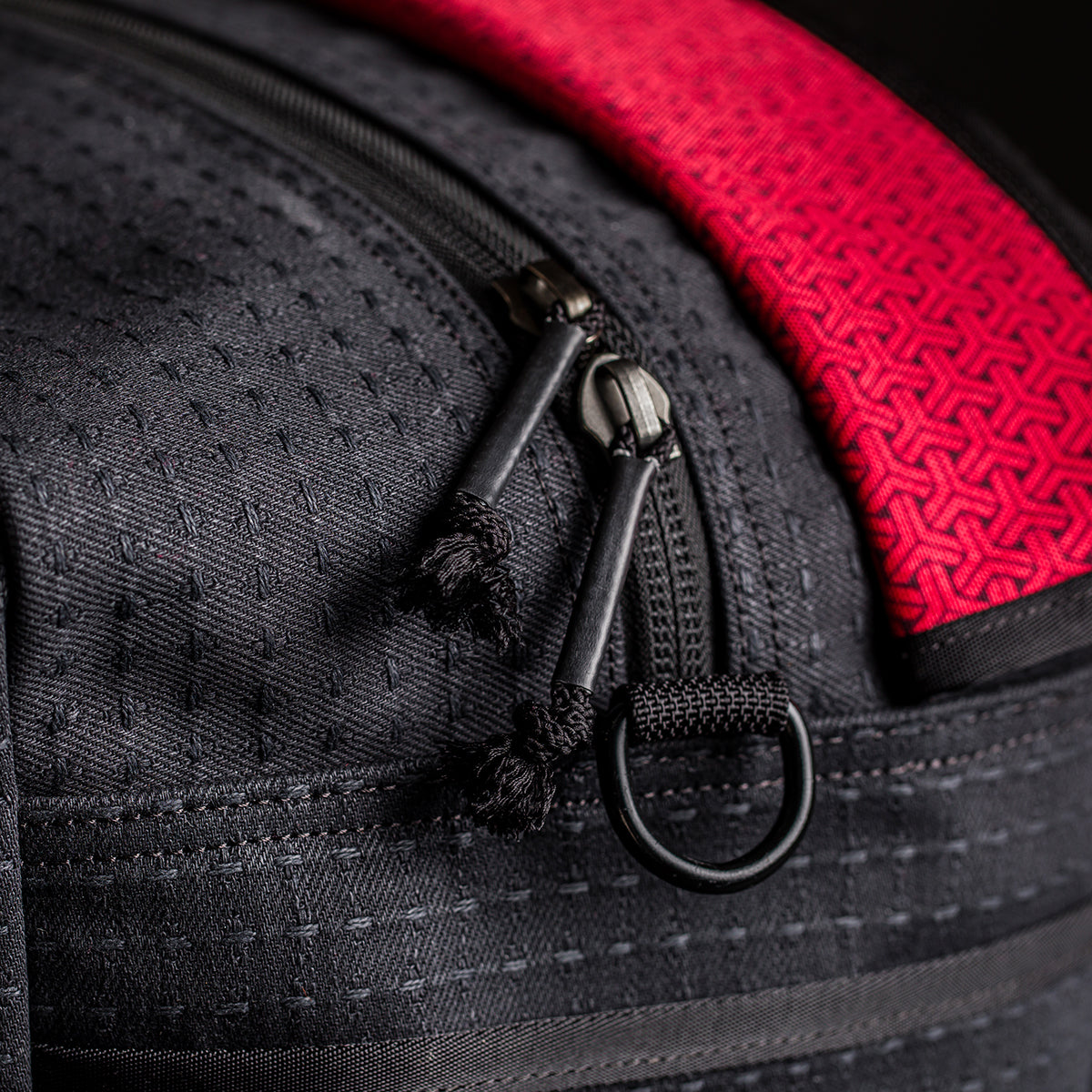 Close-up of black Kit Bag x Carryology - GRXC2 Samurai 2.0 zippers, textured red strap, detailed stitching, and custom technical fabric.