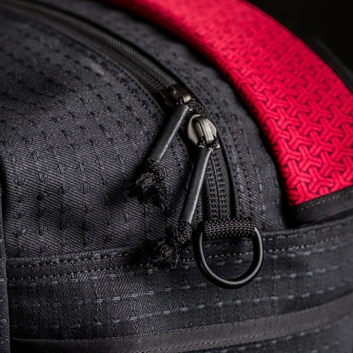 Close-up of black Kit Bag x Carryology - GRXC2 Samurai 2.0 zippers, textured red strap, detailed stitching, and custom technical fabric.