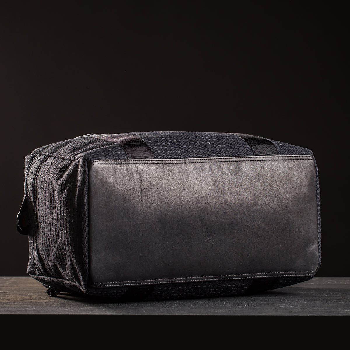 The Kit Bag x Carryology - GRXC2 Samurai 2.0, a black rectangular duffel, lies on its side against a dark background, displaying its custom technical fabric bottom panel.
