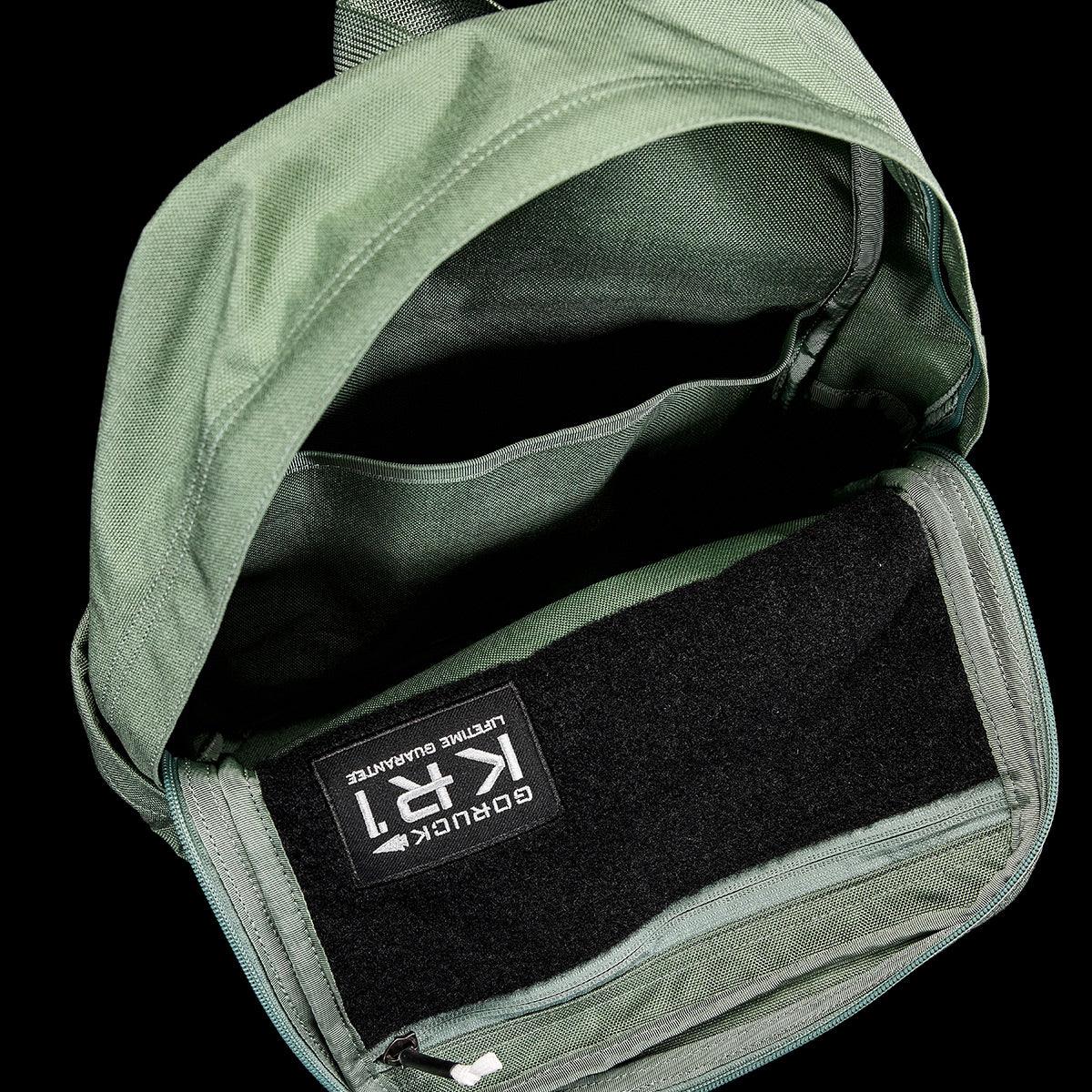 Open green 13L Kid Ruck backpack showing interior compartments and GORUCK label on black fabric
