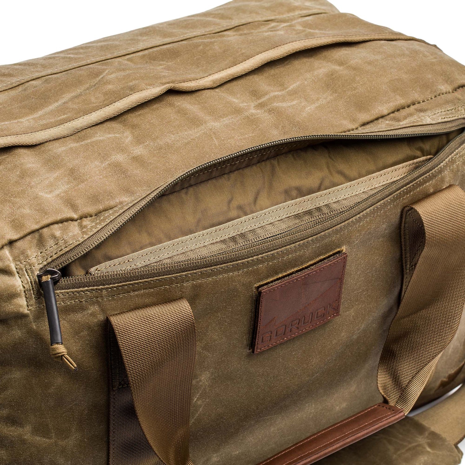 The Kit Bag - Waxed Canvas is a tan flight bag with brown handles and a front zippered pocket that is partially unzipped.