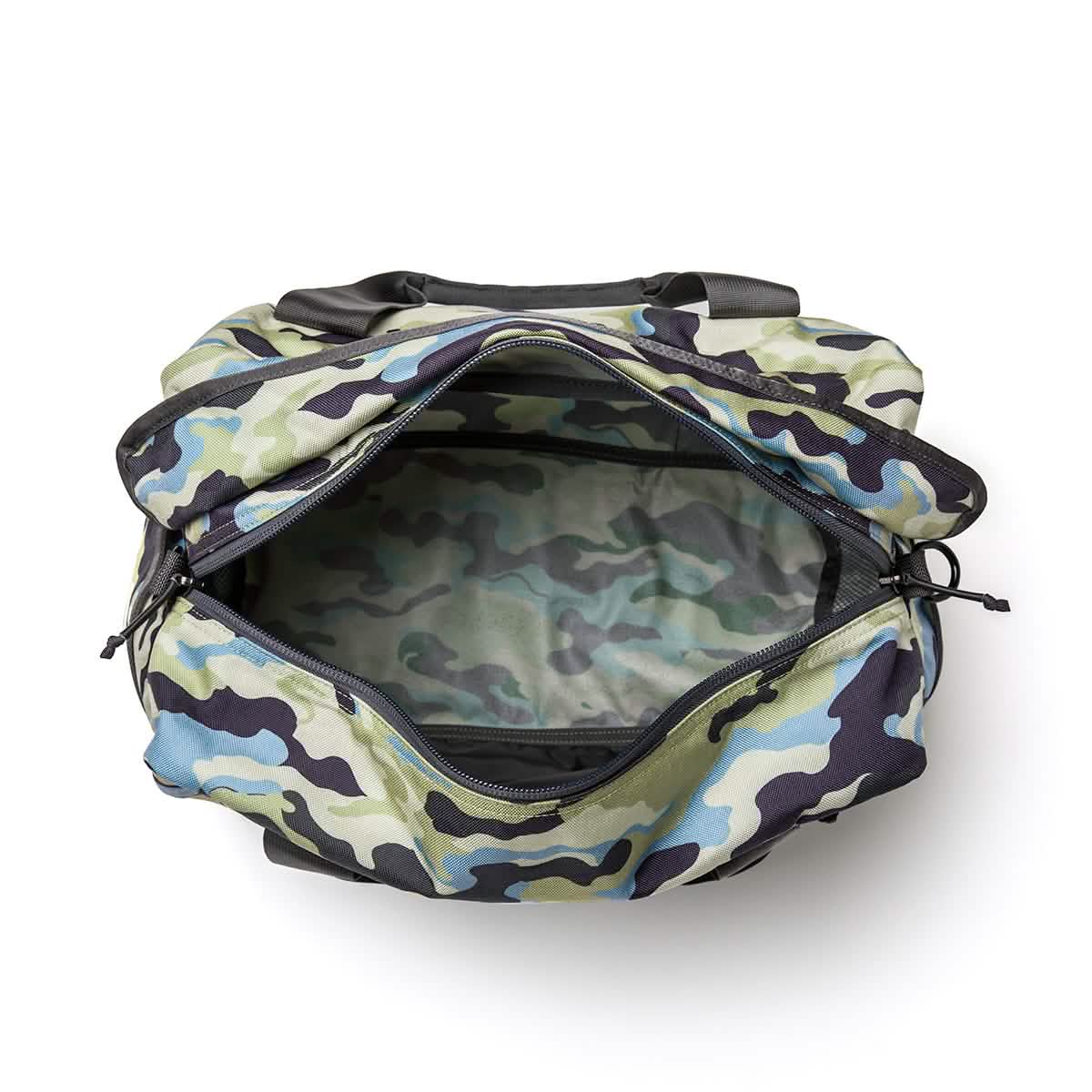 The Kit Bag by GORUCK, with its camo-patterned design in shades of green, blue, and black, is open to reveal its spacious interior. Featuring a wide zippered opening and crafted from sturdy material for durability during any mission, this deployment bag includes a shoulder strap for added convenience.