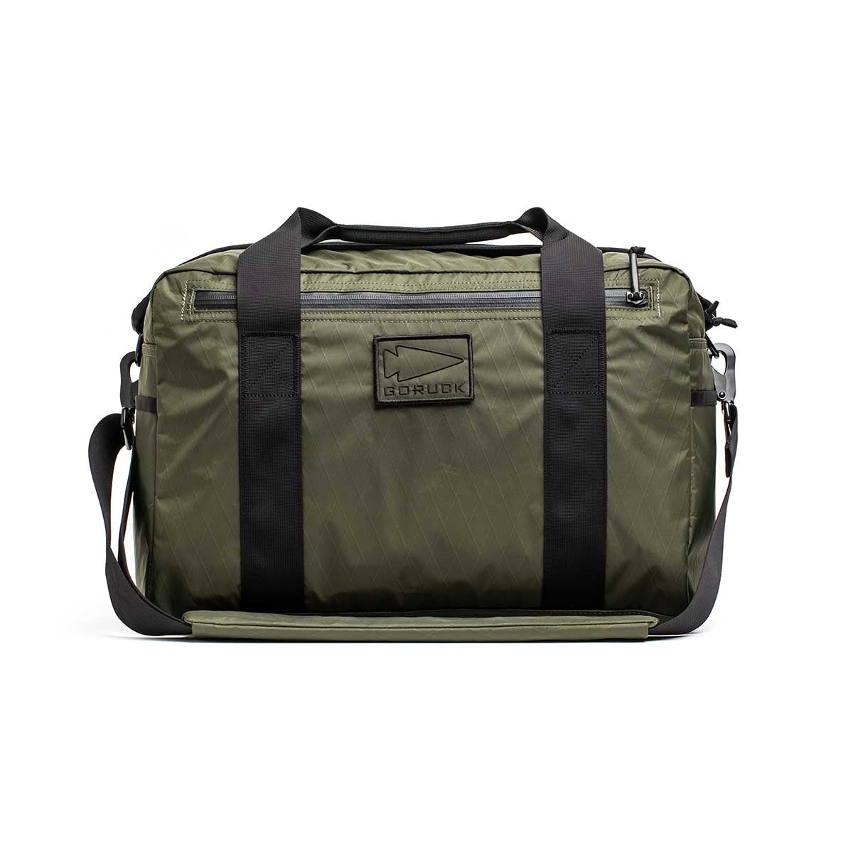 The Kit Bag - X-PAC in olive green features black straps, a front logo patch, and is made from durable X-PAC VX21 fabric, displayed against a white background.