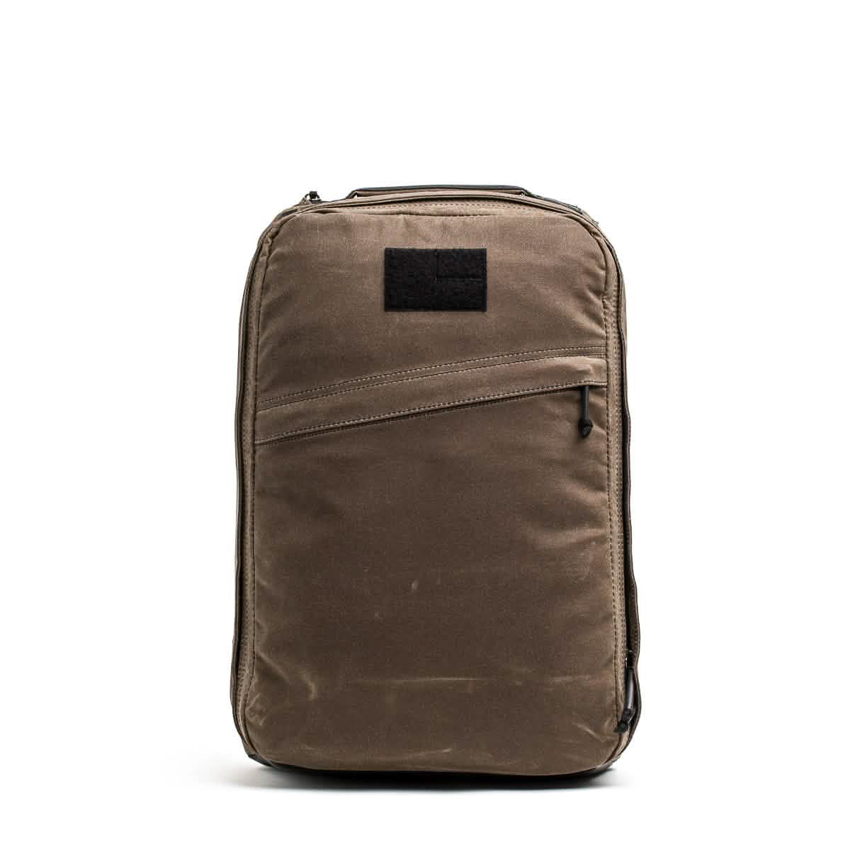 The GR1 USA - Heritage Waxed Canvas backpack features a brown rectangular design with a front diagonal zipper pocket, black patch, and top handle, shown on a white background.
