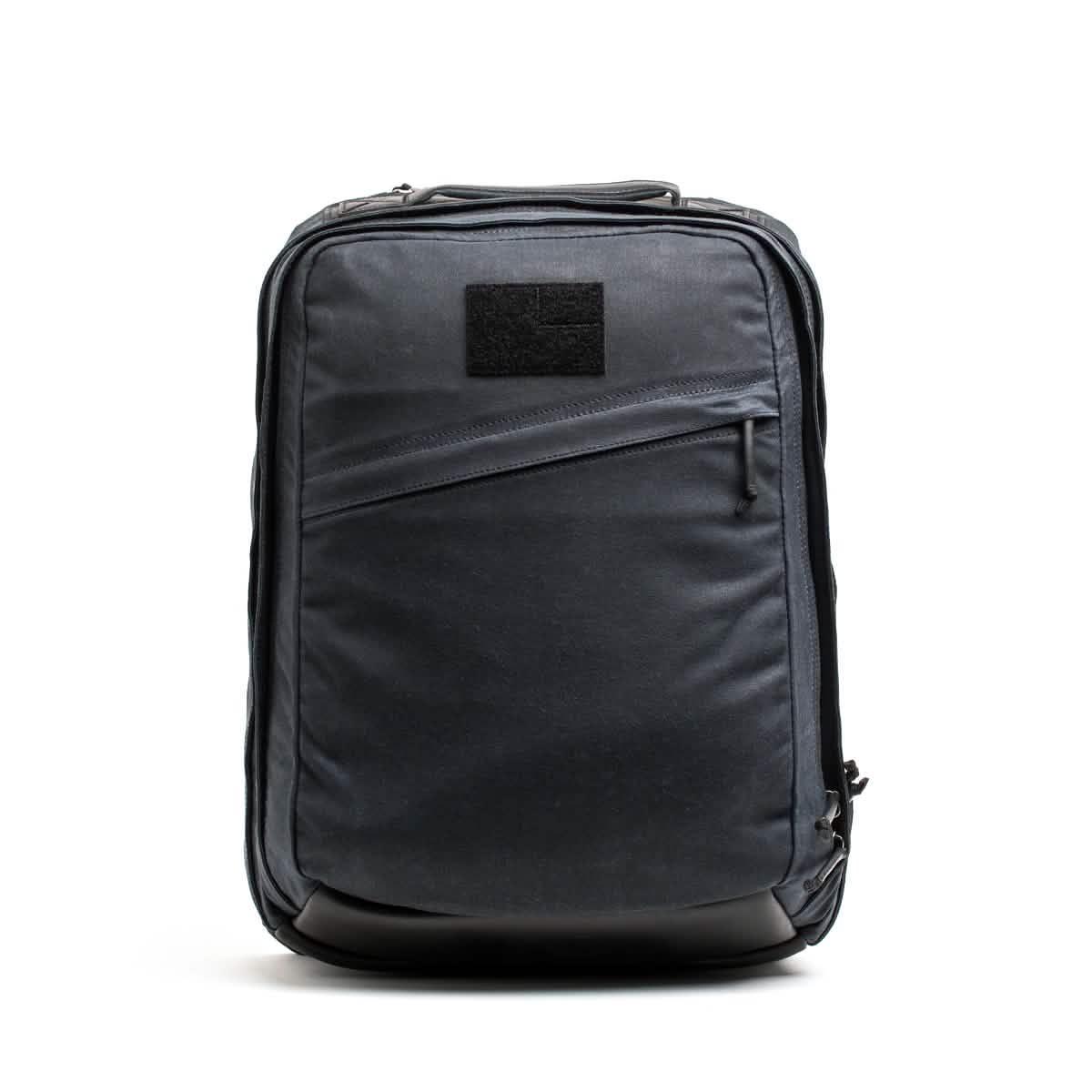 Introducing the GR2 - Waxed Canvas backpack by GORUCK: a sleek, modern black accessory crafted from durable waxed duck canvas. It features a diagonal front zipper pocket and a rectangular patch near the top, enhancing its minimalist design. The smooth fabric and subtle detailing contribute to its refined aesthetic. Photographed against a plain white background, this backpack exudes a touch of heritage retro rucksack style.