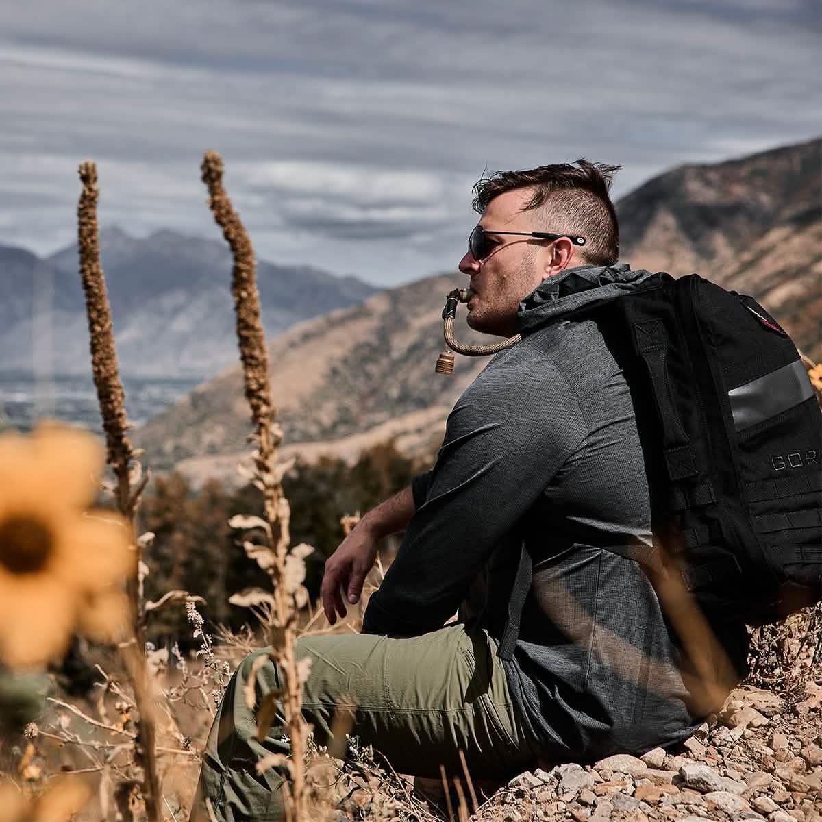 Man in GORUCK ToughMesh hoodie and backpack resting outdoors in the mountains