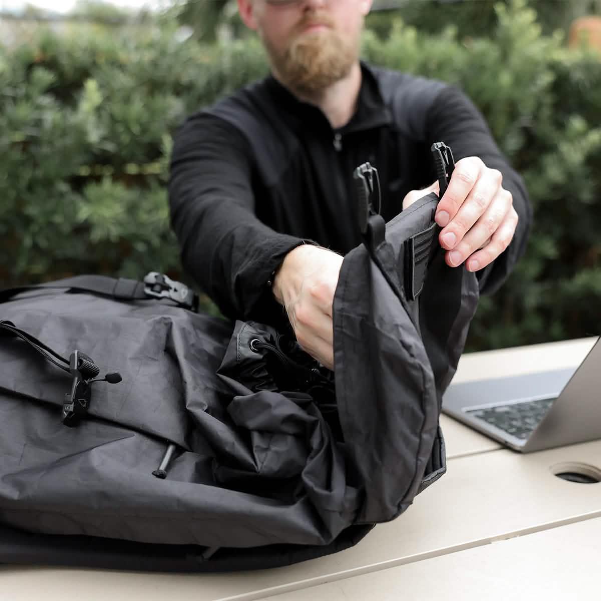 Man handling GORUCK black Dyneema rucksack at outdoor table next to laptop