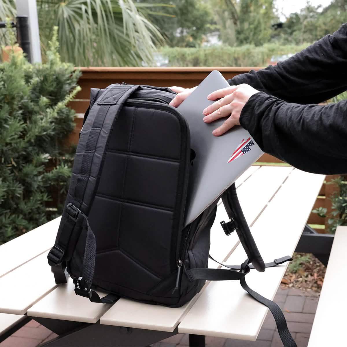 Person placing laptop into black GORUCK Dyneema rucksack on outdoor picnic table