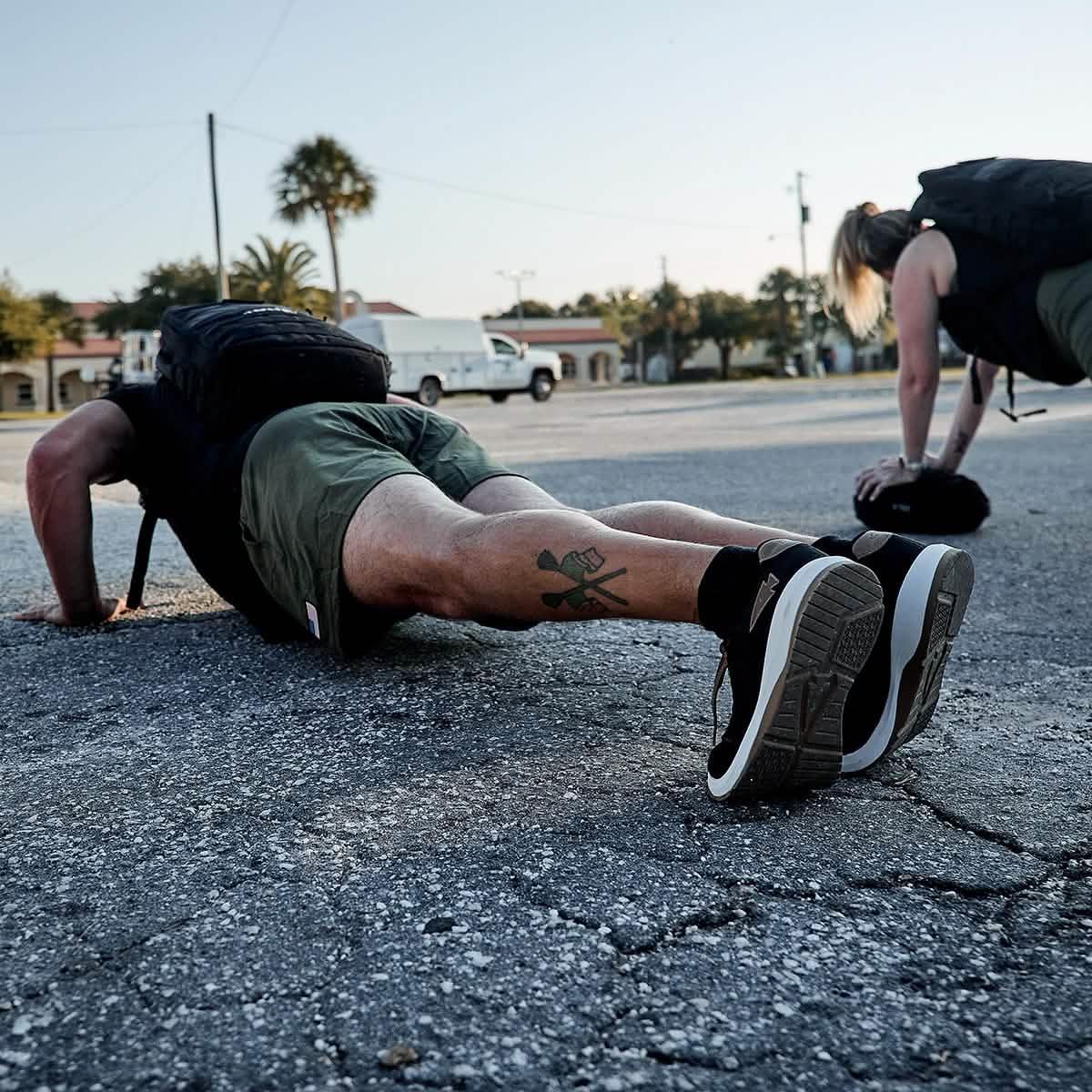 Men wearing GORUCK ballistic trainers and rucksacks doing outdoor push-ups on pavement