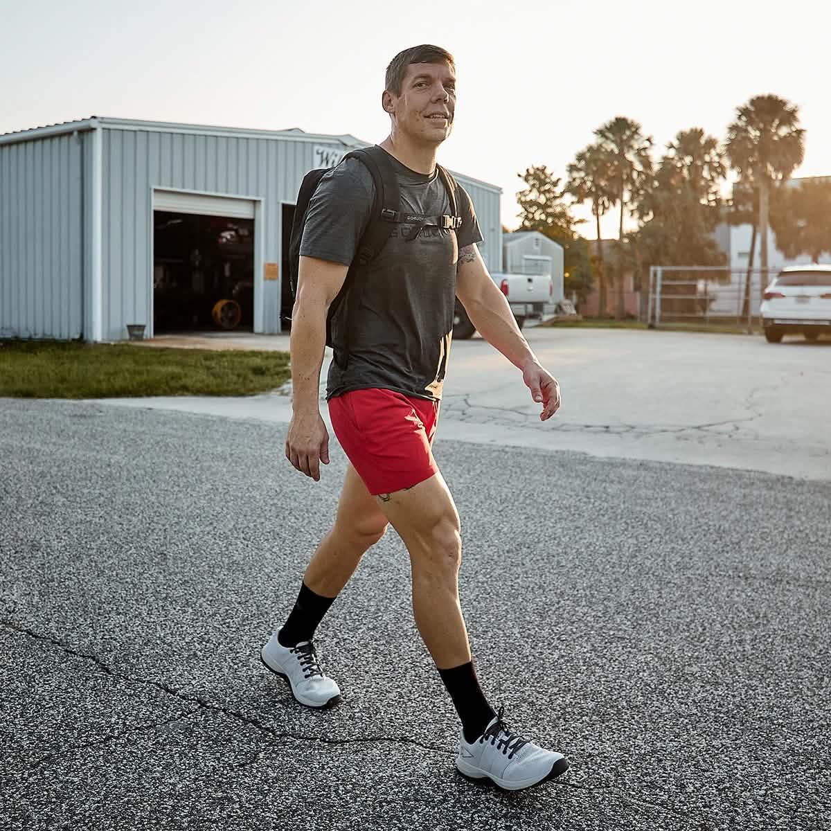 Man walking outdoors wearing GORUCK backpack, black t-shirt, red shorts, and white trainers