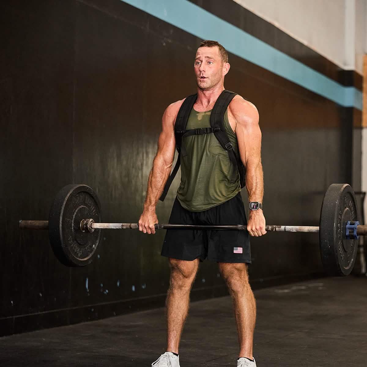 Muscular man in green tank top and black USA flag shorts lifting barbell in gym workout